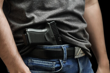 Hided handgun under the denim belt. a man in jeans and a t-shirt holds a gun in his hand from the...