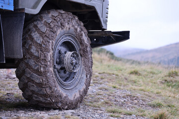 Wheel closeup in a countryside landscape with a mud road. Off-road 4x4 suv automobile with ditry body after drive in muddy road - Powered by Adobe