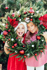 Merry Christmas. Portrait of two happy funny children girls in Santa hat with Christmas wreath. Happy Holidays. Fairy Magic. Happy kids enjoying holiday. Christmas in July