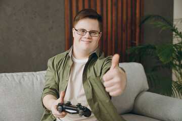 Young man with down syndrome wearing casual clothes play pc game with joystick console sits on grey...