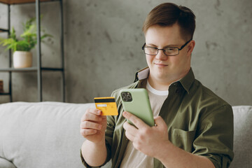 Young man with down syndrome wear casual clothes use mobile cell phone credit bank card sits on...