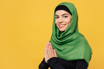 Side view young asian muslim woman wears green hijab abaya black clothes hold hand folded in prayer...
