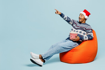 Full body young fun man wear sweater Santa hat posing sit in bag chair watch film movie point...