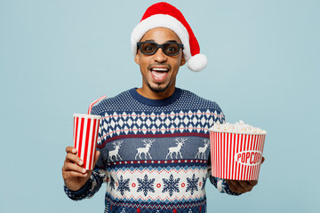 Young excited man in 3d glasses wear knitted sweater Santa hat posing watch movie film hold bucket...