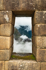 View from an ancient window in Machu Picchu. There is mountains and clouds in the background
