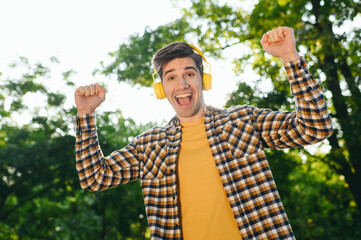 Young excited man he wearing casual clothes listen music in headphones dance walk rest relax in...
