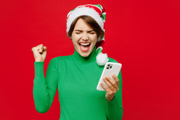 Young woman wear warm cozy green turtleneck Santa hat posing hold use mobile cell phone do winner...