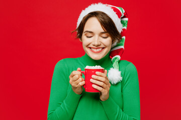 Young cheerful woman wear green turtleneck Santa hat posing drink cocoa coffee tea with tasty marshmallow isolated on plain red background. Happy New Year 2024 celebration Christmas holiday concept. - Powered by Adobe