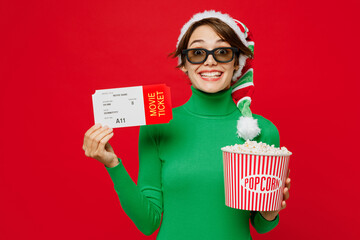 Young woman in 3d glasses wears green turtleneck Santa hat watch movie film hold in hand ticket popcorn bucket in cinema isolated on plain red background Happy New Year 2024 Christmas holiday concept - obrazy, fototapety, plakaty