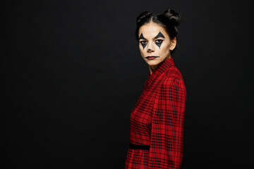 Side view serious calm young woman with Halloween makeup face art mask wear clown costume red dress look camera isolated on plain solid black background studio portrait. Scary holiday party concept.