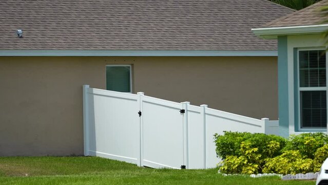 White vinyl picket fence on green lawn surrounding property grounds for backyard protection and privacy