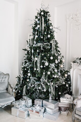 Tree with gifts boxes in white living room. Decorated Christmas interior at home. Fir-tree decorated with garlands and ball toys. Decor. Happy New Year and Merry Christmas. Concept of winter holiday.
