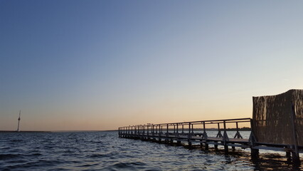 A lengthy wooden pier extends far from the shore, jutting into the calm waters of a peaceful body.