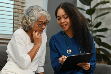 African-Asian nurse or caregiver explains the results of the health examination to the elderly woman at home. Health assessment of elderly patients in nursing homes - obrazy, fototapety, plakaty