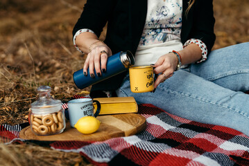 Female hands pour tea from a thermos against the backdrop of a picnic