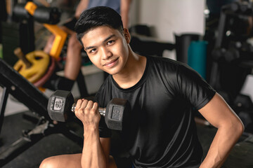 Fototapeta na wymiar A young handsome asian man looking at the camera confidently while doing concentration bicep curls on the bench. Working out at the gym.