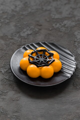 Halloween Pumpkin cream dessert, decorated with jelly cobweb, on a black plate. Dark gray background. Close up