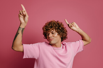 Playful young curly hair man dancing and smiling against pink background