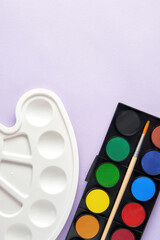 Vertical image with a watercolor paints set, brush and plastic palette on the purple surface. Drawing, arts and painting backgrounds