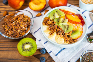 Bowl of granola with yogurt and fresh berries on a texture table. Yogurt berries, acai bowl, spirulina bowl. Healthy food, balanced breakfast. Strawberries, blueberries, kiwi, peach, almonds and chia.