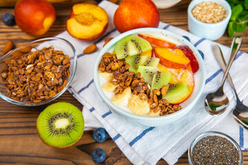 Bowl of granola with yogurt and fresh berries on a texture table. Yogurt berries, acai bowl, spirulina bowl. Healthy food, balanced breakfast. Strawberries, blueberries, kiwi, peach, almonds and chia.