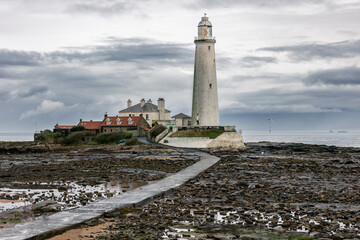 Fototapeta na wymiar St. Mary's Lighthouse with basalt path at low tide with a large offshore windmill at sea, for alternative green, renewable energy, electricity, just of the English coast. Whitley Bay, Newcastle, UK