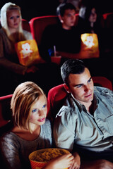 Cinema, watching and couple with popcorn, film and eating on romantic date together. Movie night, man and woman in theater with snacks, entertainment and sitting in auditorium to relax at premier.