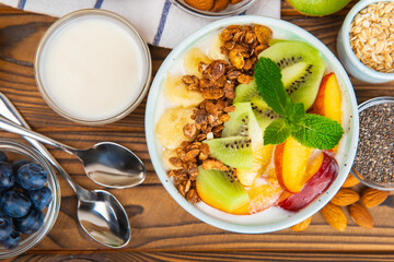 Bowl of granola with yogurt and fresh berries on a texture table. Yogurt berries, acai bowl, spirulina bowl. Healthy food, balanced breakfast. Strawberries, blueberries, kiwi, peach, almonds and chia.