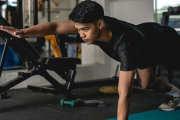 A young handsome asian man executes a prone two point bridge exercise on the mat at the gym. Advanced and difficult core exercises. - obrazy, fototapety, plakaty