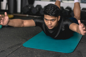 A young handsome asian man does superman back extension exercises while lying prone on a mat at the...