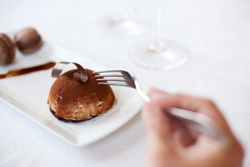 Hand, fork and eating chocolate dessert at restaurant, fine dining and food at cafe table. Closeup, mousse cake on plate and person hungry for luxury breakfast meal, cacao sugar or sweets in bakery