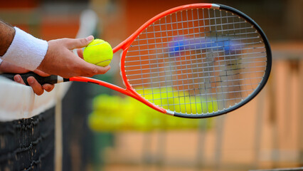 Detail of a tennis player's hand with white wristbands resting on the net, tennis ball and racket with the court blurred in the background - obrazy, fototapety, plakaty