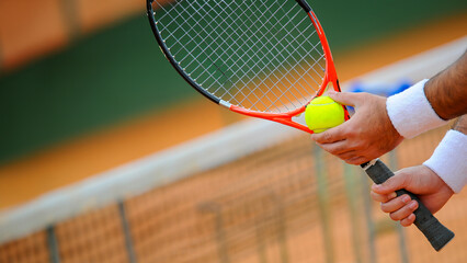 Detail of a tennis player's hand with white wristbands resting on the net, tennis ball and racket...