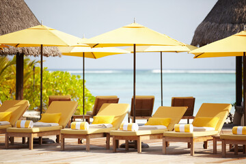 Obraz premium Maldives, deck chairs and umbrella on beach for luxury, travel or summer villa for vacation or holiday. Tropical, leisure and ocean for resort, relax and island with sunshine, outdoor or caribbean