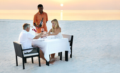 Couple, beach and dinner in sunset with waiter for romantic outdoor date, valentines day or...
