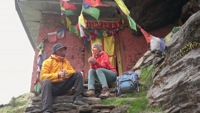 Backpackers Couple at Small Buddhist monastery decorated multicolored Tibetan prayer flags with mantras on climbing Mera peak route in Makalu Barun National Park. Peaceful and sacred place 4K video
