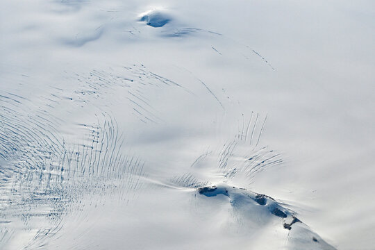Aerial view of mountains, snow fields, crevasses and glaciers of southern Greenland from airplane window on clear sunny autumn day. - Powered by Adobe