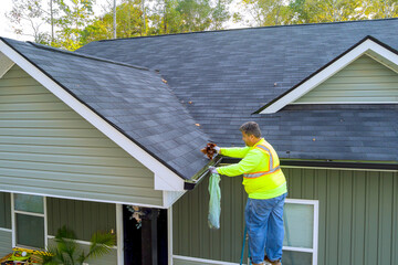 Worker is cleaning clogged roof gutter from dirt, debris fallen leaves to prevent water let...