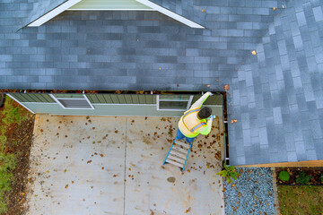 An employee is cleaning clogged roof gutter drain with dirt, debris, fallen leaves - obrazy, fototapety, plakaty