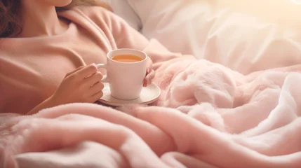 Fotobehang Woman lying in bed with warm blanket in pink colors, holding a cup of tea. Natural cold remedies. Banner. © Nataliia
