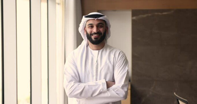 Portrait of Indian company owner, Arabian businessman in traditional Islamic attire, wear kandura and headscarf pose with arms-crossed in office, smile look at camera feel happy with business success
