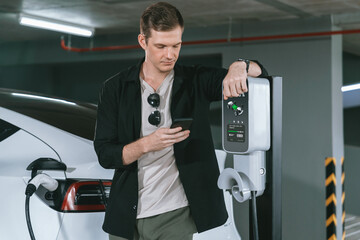 Young man travel with EV electric car to shopping center parking lot charging in downtown city...