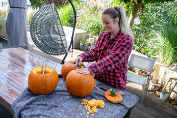 Blonde woman opening the top of a pumpkin for carving halloween decorations with a knife