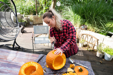 For Halloween, a blonde woman cuts a face into an orange pumpkin with a knive