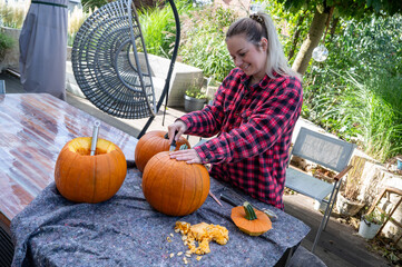 Blonde woman opening the top of a pumpkin for carving halloween decorations with a knife