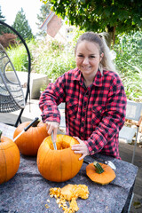 Blonde woman hollowing out and removing seeds from pumpkins as a decoration for the Halloween season