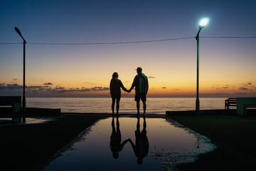Silhouette of a man and a woman holding hands and looking at the sunset
