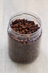 A portrait of a plastic pot or jar full of fresh dried loose buckthorn tea in it. The herb is ready to be used in a relaxing cup of the warm beverage or drink for some zen time.