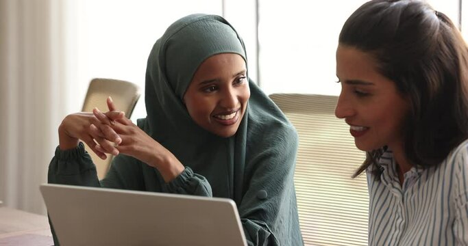 Close up beautiful multicultural marketers businesswomen, friendly colleagues lead talk sit at desk with laptop, share ideas, planning marketing ploy, discuss on-line presentation working in office