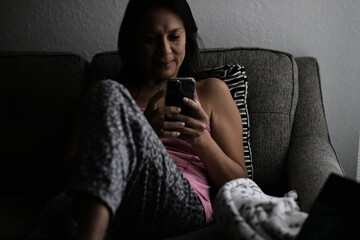 Mature woman holding a phone lying on the couch early in the morning on pajamas.